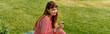 © Bliss - Young female student relaxing outdoors while engaged with her smartphone in a serene green setting