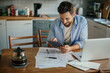 © Geber86 - Young man using a digital tablet in the kitchen while going over his bills