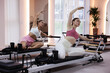 © New Africa - Woman and pilates instructor exercising on reformers in studio