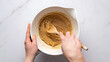 © SkNur - Overhead Close-Up of Hands Stirring Cookie Dough in White Ceramic Bowl on Marble Countertop.