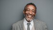 © Johannes - portrait of successful black businessman standing against grey wall smilng senior entrepreneur in formal clothing looking at camera mature happy man isolated on grey background with copy space no log