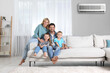 © New Africa - Happy family with children on sofa at home. Air conditioner keeping comfortable temperature in room