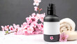 © ThabakStudio - Serene Spa Set Up: A visually appealing composition of a black lotion bottle with a blank label and pink flowers, accompanied by a rolled towel and soap, evoking tranquility and self-care.