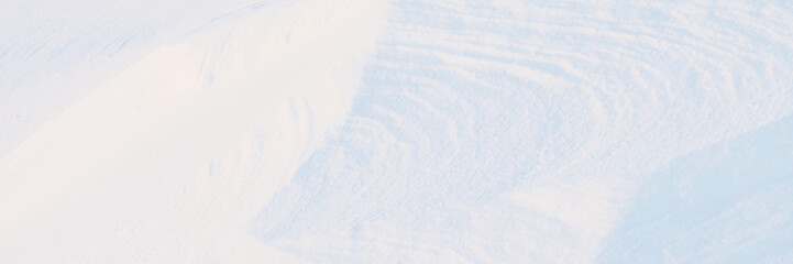 Wall Mural - Wide panoramic winter background with snowy ground. Natural snow texture. Wind sculpted patterns on snow surface.