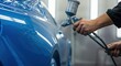 © LiaSyafitri - Automotive refinishing skilled worker sprays blue paint on car body with spray gun