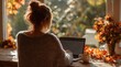 © Valentina Studio - A Cozy Autumn Scene Featuring a Young Woman Working on a Laptop by a Sunlit Window Surrounded by Fall Leaves and a Warm Cup of Coffee