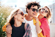 © halayalex - Group of young three stylish friends posing in the street. Fashion man and two cute female dressed in casual summer clothes. Smiling models having fun. Cheerful women and guy outdoors, sunglasses