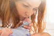 © pressmaster - Caucasian young adult woman gently holding newborn baby hand while gazing closely at infant face, showing tender interaction between mother and child in bright indoor setting