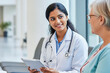 © UniqGraphicX - Indian Female Medical Doctor Smiling and Talking to Senior Patient While Holding Tablet