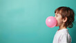 © Vadym - Young boy blows large pink bubble gum. Profile view captures childs enjoyment with candy on turquoise studio backdrop. Playful kid expresses happiness, youth, innocence.