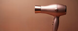 Rose gold hairdryer on brown background. Metallic copper electric appliance. Modern stylish dryer tool for salon, home hair styling. Beauty device for hair care, grooming. Hairdresser equipment,
