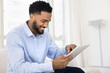 © fizkes - Smiling young man resting on sofa with digital tablet