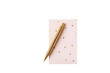 © Guds - A gold pen resting on a pink notebook with gold polka dots