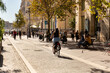 © Simplementbeau. - Vélo en ville, jeune femme à vélo au premier plan vue de dos sur une piste cyclable du centre ville de Marseille, promeneurs et allée d’arbres au second plan