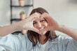 © Daniel - Beautiful woman showing heart sign with folded fingers smiling looking at camera, head shot portrait. Attractive optimistic young female demonstrate symbol of love feels happy posing alone at home