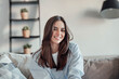 © Daniel - Young attractive cheerful lady sitting on sofa, relaxing looking at the camera at home. Beautiful brunette woman on her 30s chatting on video call online