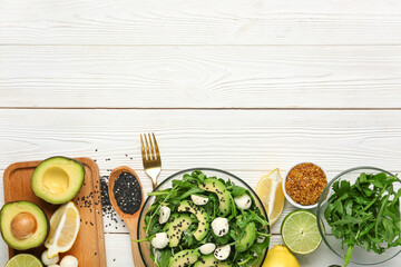 Wall Mural - Bowl with healthy arugula salad and ingredients on white wooden background