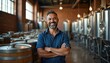 © Viktor - Hispanic brewery owner smiles confidently arms crossed near beer kegs and fermentation tanks. Mature businessman in casual attire represents successful small business in craft beer industry.