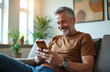 © Viktor - Happy middle aged man uses smartphone for online shopping at home. Adds credit card to mobile wallet, paying for purchases electronically. Modern lifestyle embraces convenient e-commerce, digital