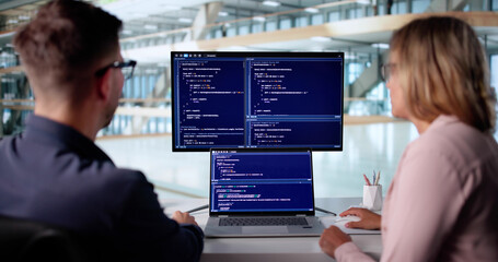 Male Developer Typing Code On Laptop With Female Trainee