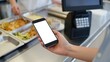 © Jessika Cahya - A person holding a smartphone in a busy cafeteria, likely for ordering or paying.