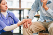 © kenchiro168 - Young healthcare worker comforting patient by holding hand in clinic, compassionate support and calm reassurance