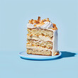 © Taina - A slice of layered coconut cake with white frosting and toasted coconut flakes on a blue plate against a light blue background