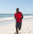 © wavebreak3 - Man jogging on sandy beach, enjoying sunny day and ocean breeze, copy space