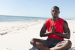 © wavebreak3 - Meditating on beach, African American man in red shirt enjoying peaceful moment, copy space