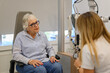 © Moon Safari - Senior woman sharing her eye problems with female doctor while sitting by eye test equipment in examination room