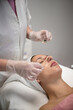 © AnastasiiaAkh - Beautician applying cosmetic treatment on female face with cotton swab in beauty salon