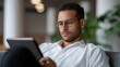 © Kateryna - Young Hispanic man in glasses working on a digital tablet while lounging on an office couch his workspace modern and airy tablet office work Hispanic professional modern
