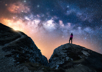 Wall Mural - Glowing Milky Way and woman on mountain peak at starry night. Dolomites, Italy. Galaxy. Space landscape with silhouette of a girl, rocks, trail, sky with bright stars. Milky Way and hiker. Nightscape