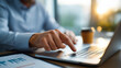 © Kateryna - A businessman points to a KPI icon on a laptop surrounded by performance graphs his desk with a notepad and a coffee cup sunlight streaming in KPI evaluation business