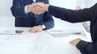 © volha_r - Business partners shaking hands at a meeting, celebrating successful negotiations and signing a contract, with documents, digital tablet, and smartphone on the table