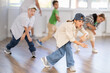 © JackF - Happy enthusiastic teen girl honing hip-hop moves in modern dance studio setting with group of children