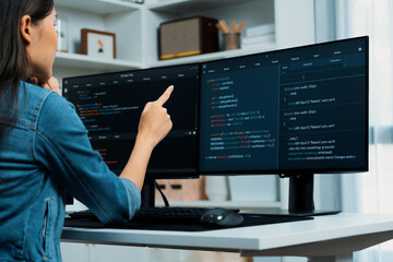 Young Asian girl of IT developer pointing online information on pc with coding program data application on website project, wearing jeans shirt. surrounded by safety programing two screens. Stratagem.