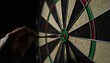© fara - Hand holding a dart that perfectly hit the bullseye on a dark, textured dartboard, symbolizing achievement, focus, and precision in sport.