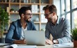 © James - Two busy diverse male employees using laptop computer talking in office. Professional young business men workers team having conversation working on project sharing ideas sitting at work desk.