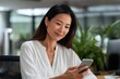 © Iryna - Asian female adult using smartphone in modern office setting