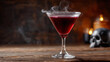 © AucArtStudio - Smoky red cocktail drink in glass on wooden table with halloween skull and candle creating spooky atmosphere for celebration