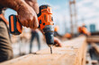 © Alina - A construction worker in safety gear drills into a wooden plank during sunset at a bustling construction site.