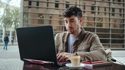 Young Freelancer entrepreneur working on a laptop at outdoor cafe in the city