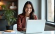 © Maria - Vertical portrait of confident businesswoman leader in her 30s at work desk. Smiling Hispanic young woman entrepreneur, happy female executive manager looking at camera sitting at work with laptop.