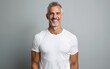 © David - Happy confident handsome fit sporty healthy mature older man, middle aged sportsman athlete or personal trainer wearing white t-shirt standing isolated on gray background advertising gym. Portrait