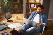 © Stockphotodirectors - A person is seated at a wooden desk in a home office, working on a laptop with feet up, sipping a beverage, and surrounded by plants and natural light for a warm atmosphere.