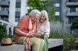 © Halfpoint - Elderly mother sitting on bench with adult daughter, reading together.