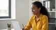 © Tams - Smiling woman working on a laptop at desk in bright office space