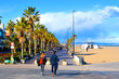People  walk on path at coastline in autumn holiday season. Winter season in Spain. Couple walking at seafront with Palm trees of La Marina de Valencia. Tourists stroll  coastline on weekend in Spain.