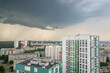 Ominous storm clouds loom above a city skyline as rain starts to fall. Residential and commercial buildings stretch across the urban area, with greenery visible beyond. bird's eye view, aerial view